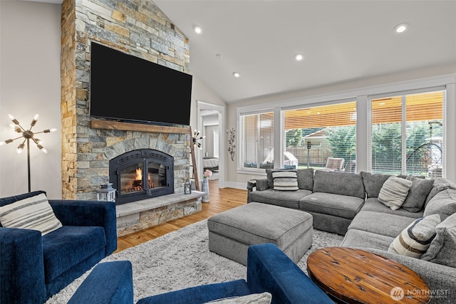 living room featuring baseboards, wood finished floors, vaulted ceiling, a stone fireplace, and recessed lighting