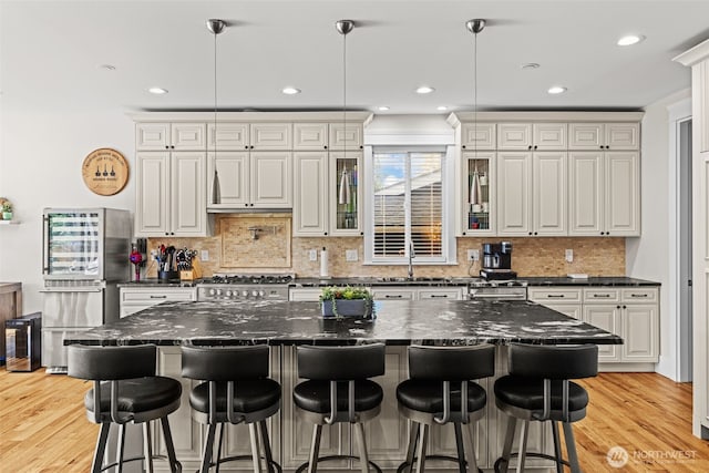 kitchen with glass insert cabinets, decorative light fixtures, and light wood finished floors