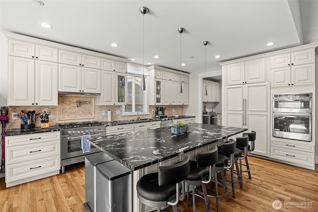 kitchen with premium appliances, white cabinetry, light wood-style flooring, and a breakfast bar area