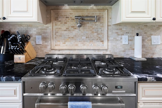 interior details featuring stainless steel gas range, tasteful backsplash, white cabinets, and dark stone countertops