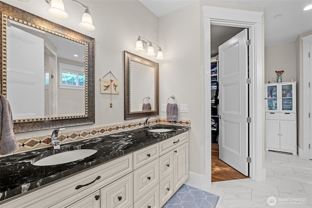 bathroom featuring double vanity, marble finish floor, a walk in closet, and a sink