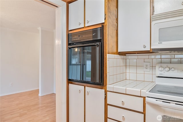 kitchen featuring white appliances, white cabinets, tile counters, tasteful backsplash, and crown molding