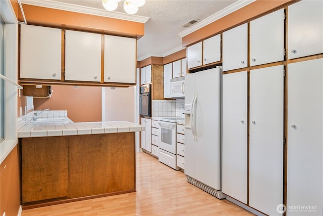 kitchen with crown molding, tile counters, visible vents, white cabinetry, and white appliances