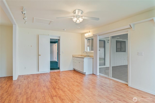 empty room with light wood-type flooring, a sink, attic access, and a ceiling fan