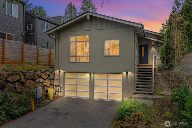 view of front of home featuring aphalt driveway, stucco siding, an attached garage, and fence