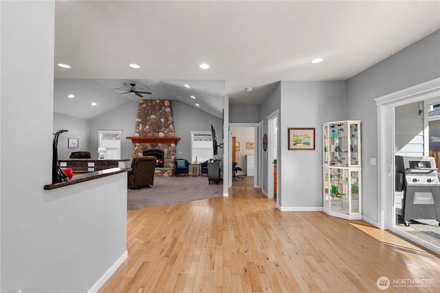 interior space featuring a ceiling fan, vaulted ceiling, a stone fireplace, light wood-style floors, and recessed lighting