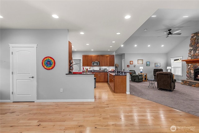 kitchen featuring brown cabinetry, dark countertops, stainless steel microwave, open floor plan, and a peninsula