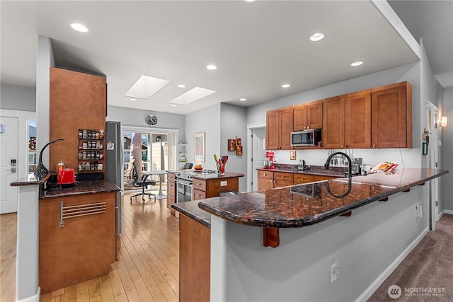 kitchen with a peninsula, brown cabinetry, dark stone counters, and stainless steel appliances