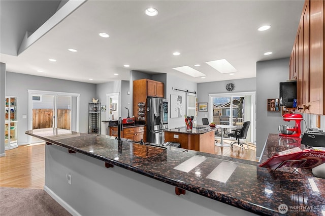 kitchen featuring a center island, a skylight, brown cabinets, a barn door, and stainless steel fridge with ice dispenser