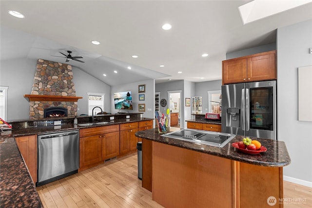 kitchen with a stone fireplace, stainless steel appliances, a kitchen island, a sink, and light wood-type flooring