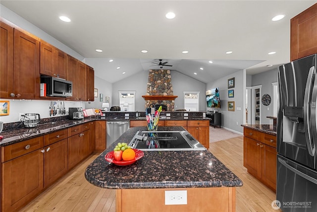 kitchen with light wood finished floors, a kitchen island, a peninsula, stainless steel appliances, and a fireplace