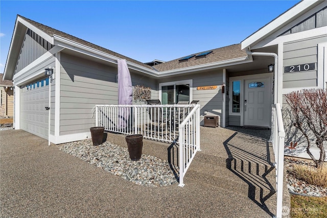 entrance to property featuring a garage, roof with shingles, and board and batten siding