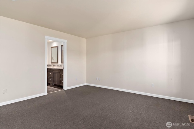 unfurnished bedroom featuring dark colored carpet, visible vents, a sink, ensuite bath, and baseboards