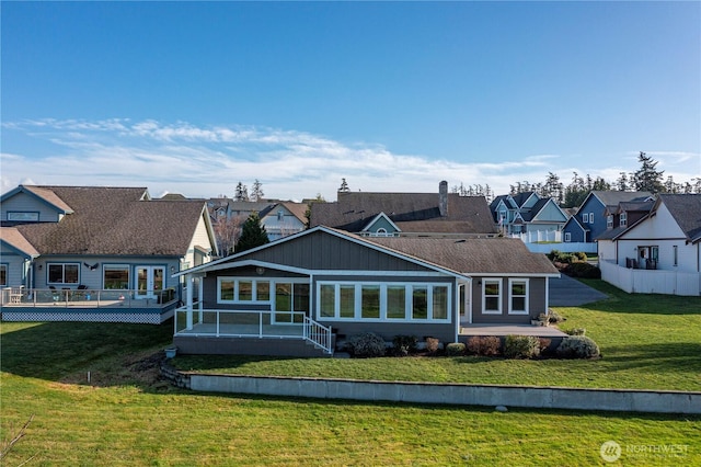 rear view of property with a sunroom, a yard, a wooden deck, and a residential view