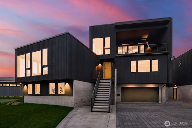 contemporary house with decorative driveway, a lawn, stairway, an attached garage, and a balcony