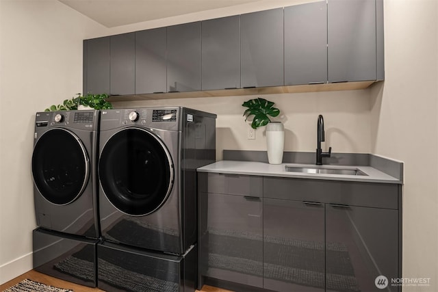 laundry area with cabinet space, baseboards, washing machine and clothes dryer, light wood-type flooring, and a sink