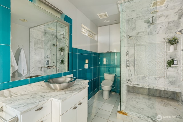 bathroom featuring visible vents, toilet, vanity, a shower stall, and tile walls