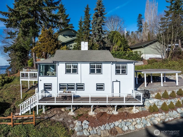 rear view of property featuring a shingled roof, a chimney, and stairs