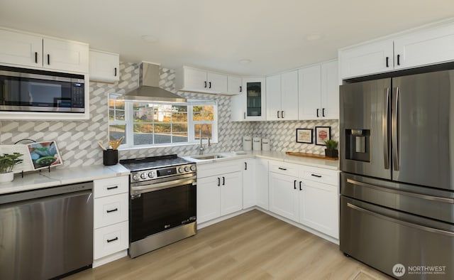 kitchen featuring stainless steel appliances, a sink, white cabinetry, light countertops, and wall chimney range hood