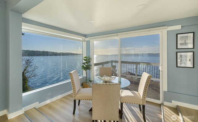 dining area featuring a water view, baseboards, and wood finished floors