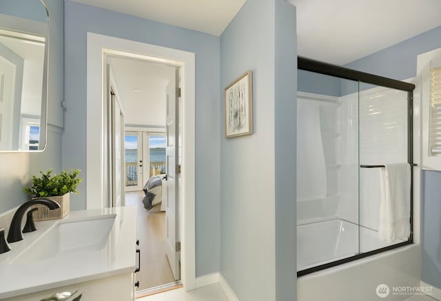 ensuite bathroom featuring vanity, ensuite bath, a shower with shower door, and baseboards