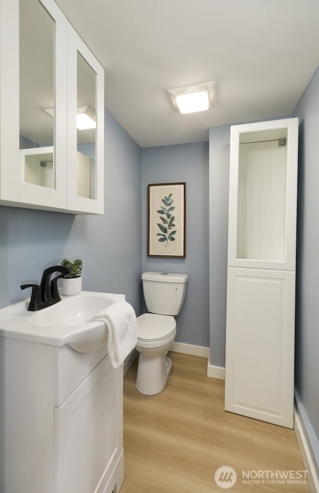 half bath with toilet, baseboards, wood finished floors, and vanity