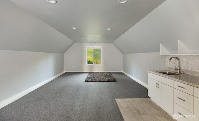 bonus room featuring lofted ceiling, a sink, light colored carpet, and baseboards