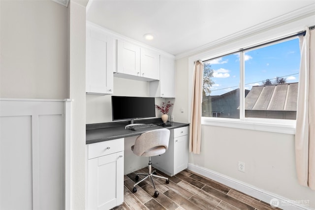 office space featuring baseboards, built in desk, wood finish floors, and crown molding