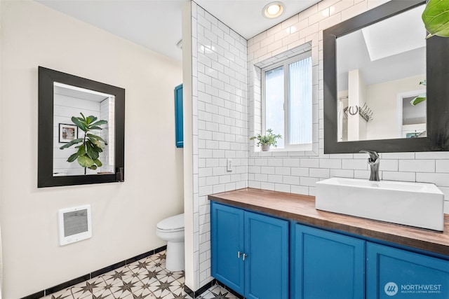 bathroom featuring toilet, baseboards, backsplash, heating unit, and vanity