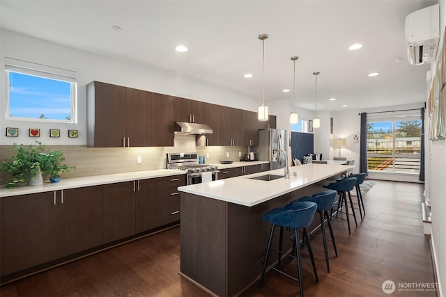 kitchen featuring a breakfast bar, stainless steel appliances, a sink, dark brown cabinetry, and under cabinet range hood