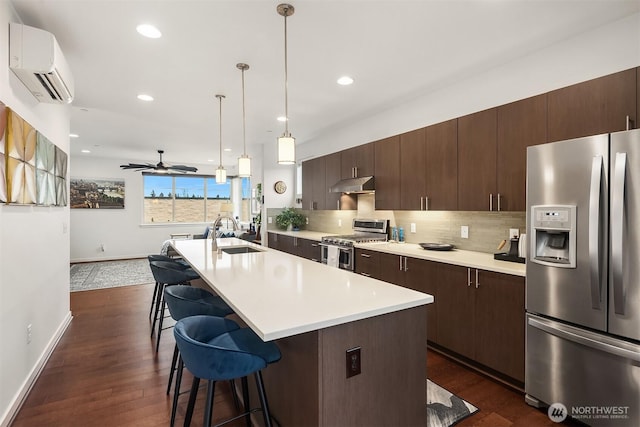 kitchen featuring tasteful backsplash, appliances with stainless steel finishes, light countertops, an AC wall unit, and under cabinet range hood