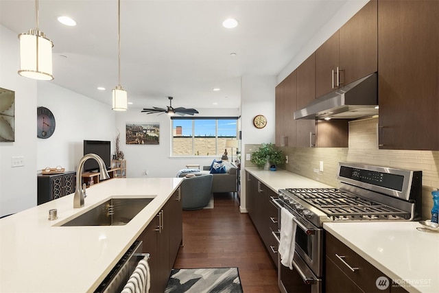 kitchen with light countertops, appliances with stainless steel finishes, open floor plan, a sink, and under cabinet range hood