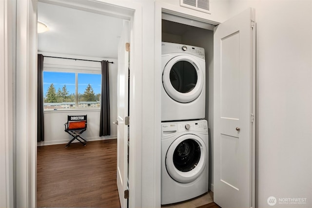 laundry area with laundry area, baseboards, visible vents, stacked washer / drying machine, and wood finished floors