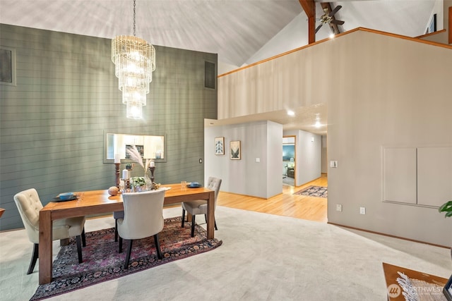 carpeted dining area with high vaulted ceiling, visible vents, wood finished floors, and ceiling fan with notable chandelier