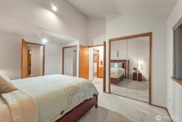 bedroom with high vaulted ceiling, light carpet, a textured ceiling, and two closets