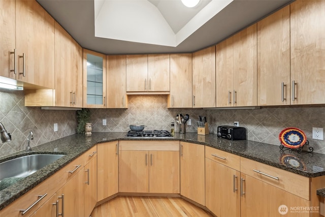 kitchen with light wood-type flooring, stainless steel gas cooktop, dark stone counters, and a sink