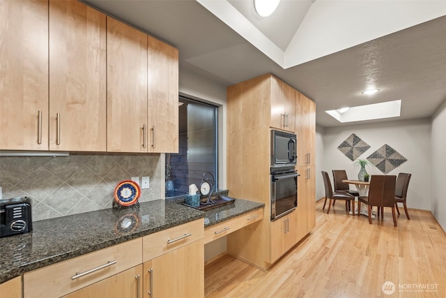 kitchen featuring backsplash, light wood-style floors, light brown cabinets, dark stone counters, and black appliances