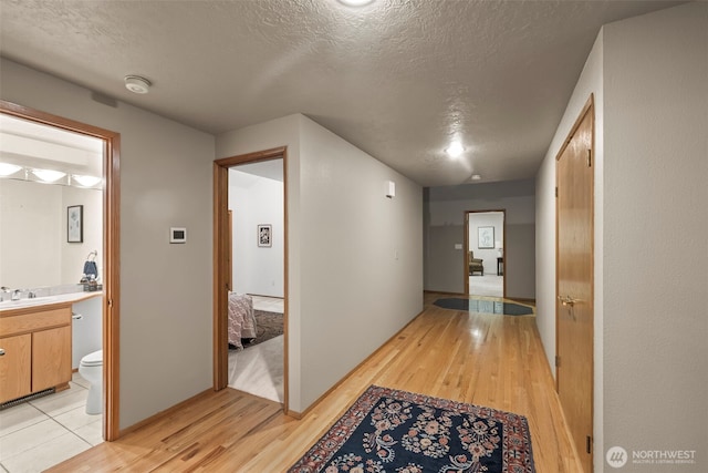 hallway featuring a sink, light wood-style flooring, and a textured ceiling