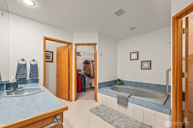 full bathroom with visible vents, a spacious closet, vanity, a bath, and tile patterned floors