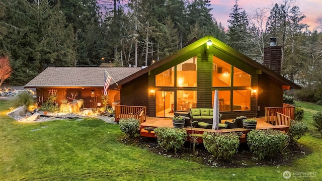 back of house at dusk featuring a lawn, a chimney, and a wooden deck