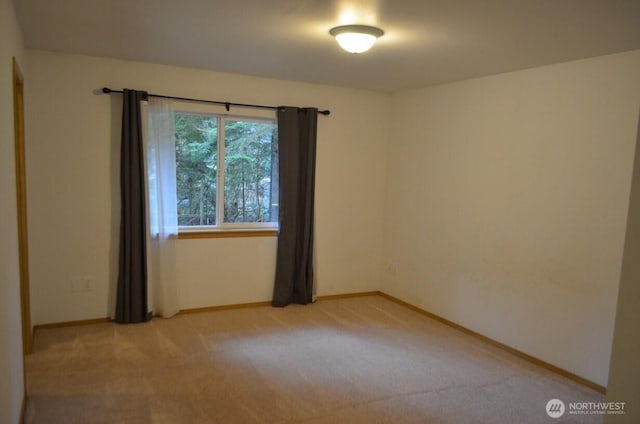 spare room featuring light carpet and baseboards