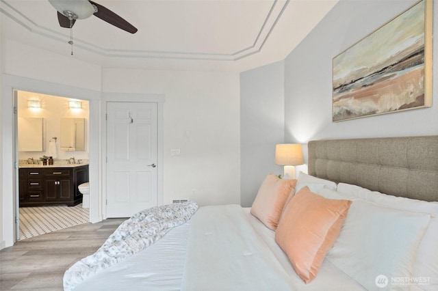 bedroom featuring a tray ceiling, light wood-style floors, connected bathroom, a sink, and ceiling fan