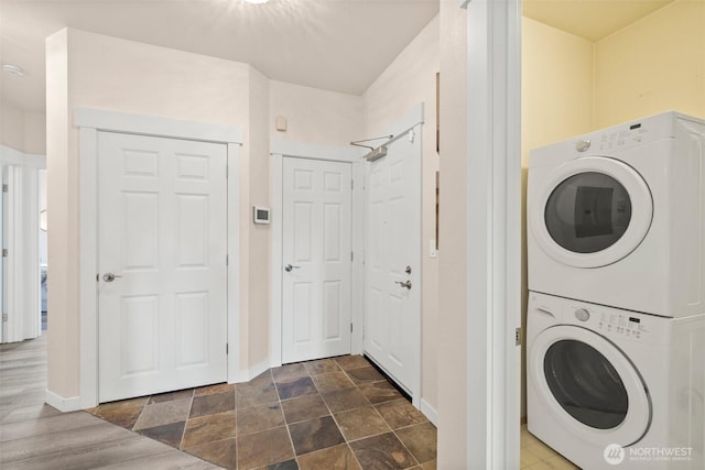 clothes washing area featuring baseboards, laundry area, and stacked washer / drying machine