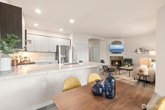 dining room featuring baseboards, arched walkways, a tiled fireplace, and recessed lighting