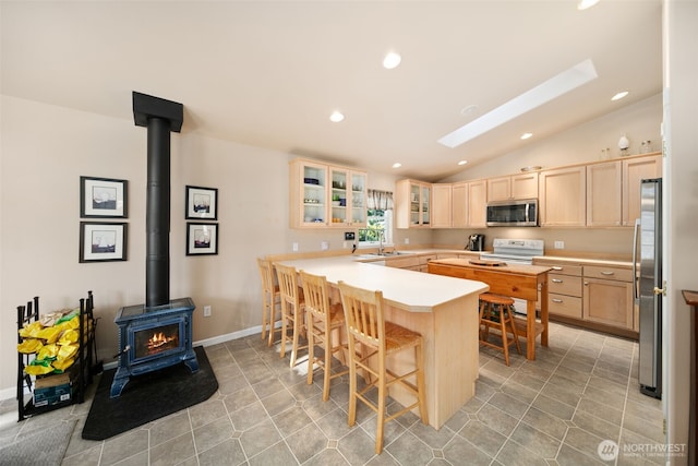 kitchen featuring glass insert cabinets, a kitchen breakfast bar, a peninsula, stainless steel appliances, and light brown cabinets