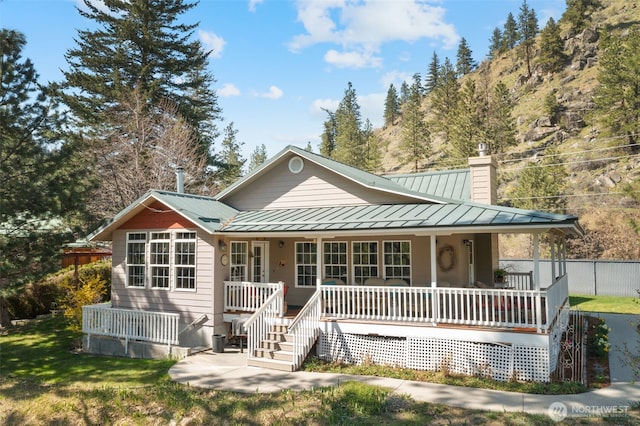 back of house with a chimney, covered porch, fence, metal roof, and a standing seam roof