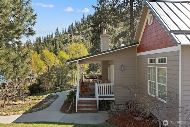 view of property exterior featuring a chimney, a standing seam roof, a deck, and metal roof