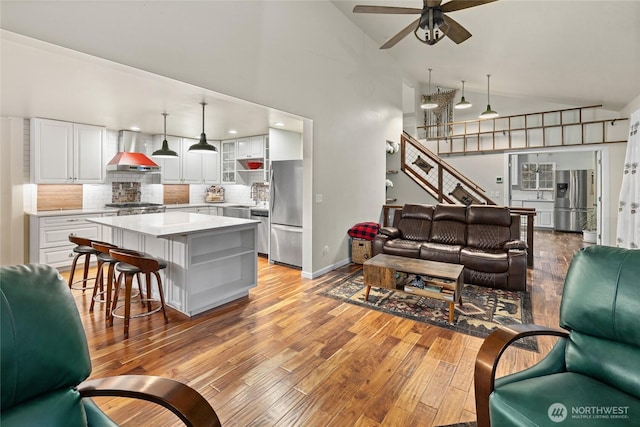 living room featuring light wood-style floors, ceiling fan, high vaulted ceiling, baseboards, and stairs