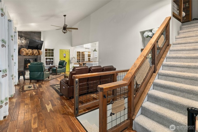 living room with ceiling fan, wood finished floors, stairs, a fireplace, and high vaulted ceiling