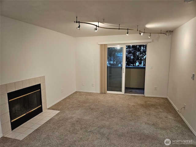 unfurnished living room featuring carpet floors, baseboards, rail lighting, and a tiled fireplace